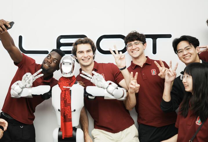 Students pose with a robot giving a peace sign.