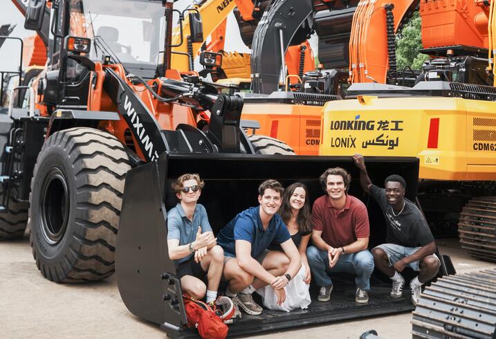 Students sit inside bulldozer shovel.
