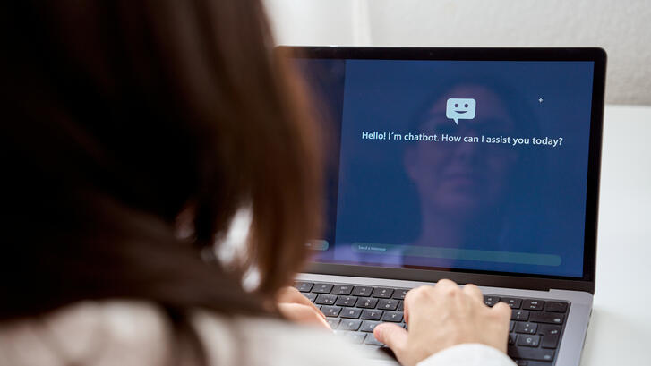 Back view of crop anonymous female talking to a chatbot of computer while sitting at home