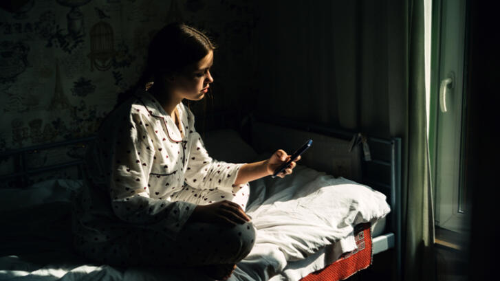 image of teen girls sitting on bed looking at phone