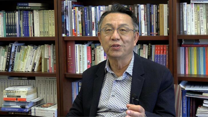 Gi-Wook Shin seated in his office, speaking to the camera during an interview.