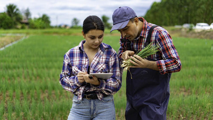 Two farmers discuss a crop issue; one is referring to a digital tablet.