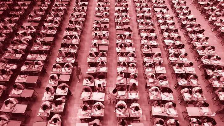Hundreds of students sit at desks in rows taking an exam.