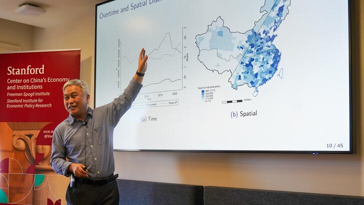 Hanming Fang presents in front of slides in a conference room.