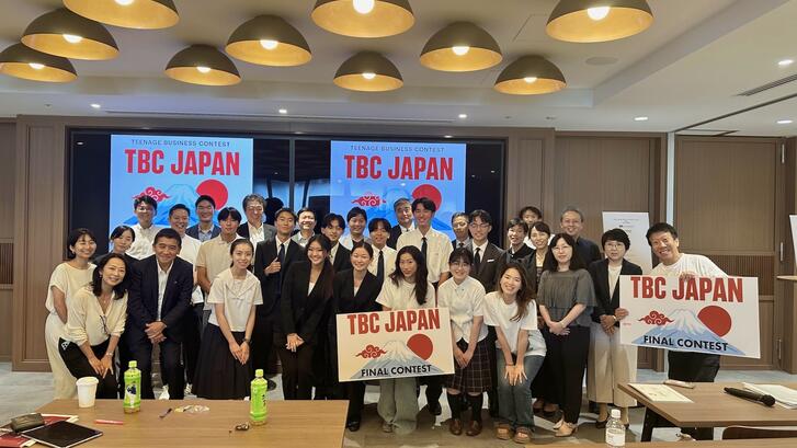 a group of students standing with signs, "TBC Japan"
