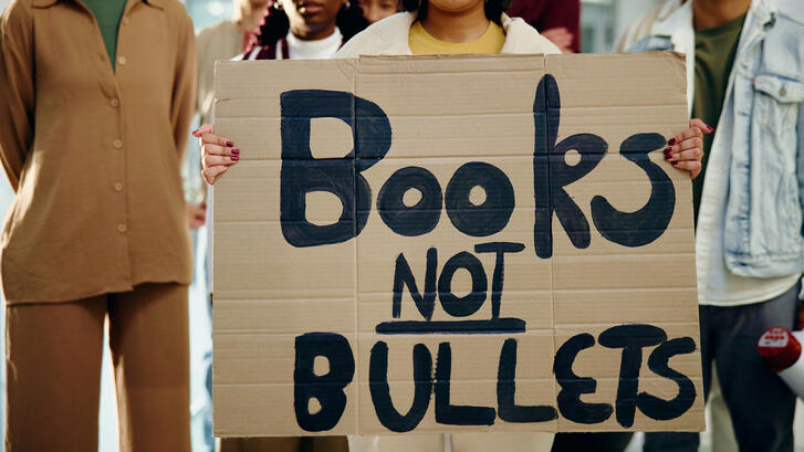 An image of students holding a protest sign that reads "Books not bullets" 