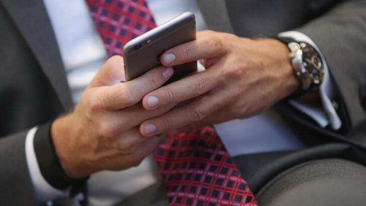 Close-up of a person in a suit and red patterned tie using a smartphone, with a wristwatch visible on their left wrist.