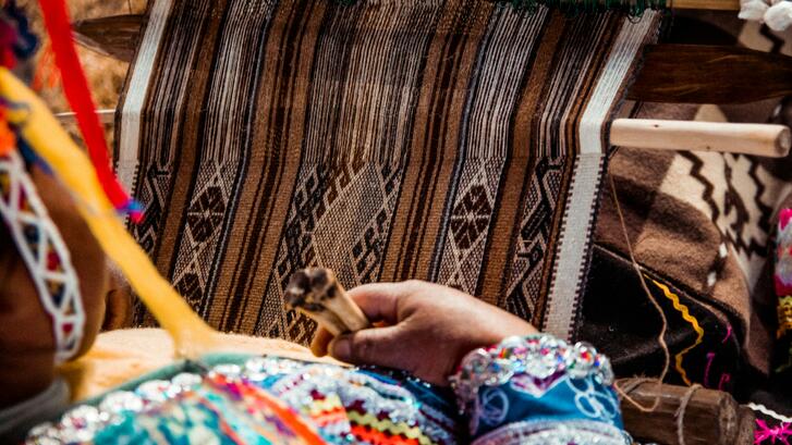 Woman working on a loom wearing traditional dress in Peru.