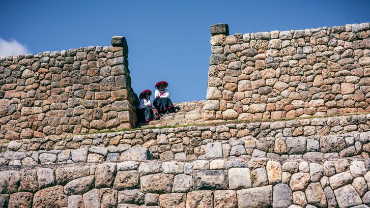 Two native women sit atop a rock wall in Peru.
