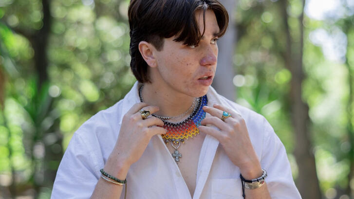 Anagali Ducan adjusting a colorful beaded necklace while standing outdoors with greenery in background.