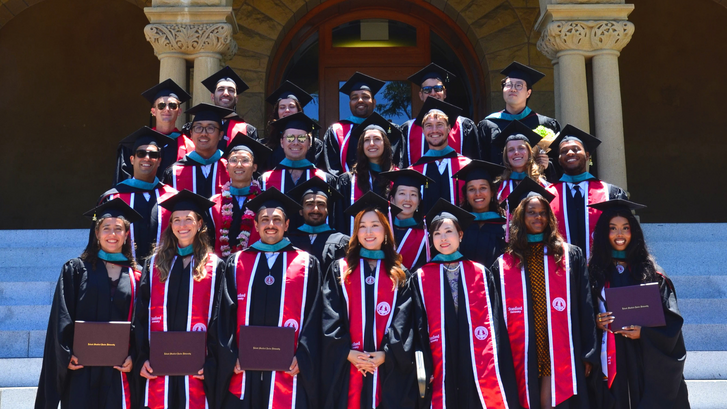 Graduates of the Ford Dorsey Master's in International Policy Class of 2026 pose on the steps of Encina Hall at Stanford University in their caps and gowns and diplomas.