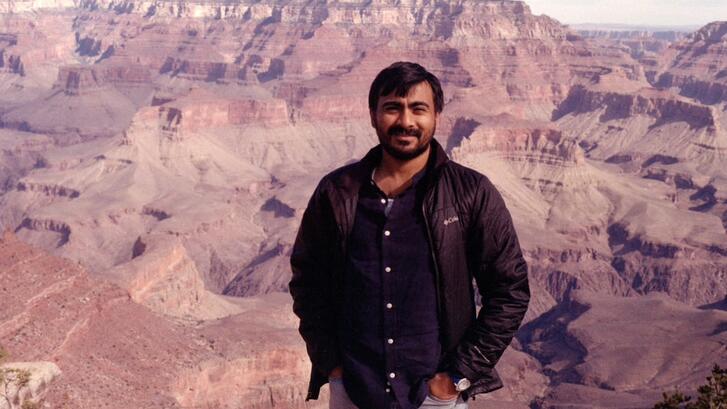 Image of Humzah Khan in a brown jacket, posing in front of the Grand Canyon