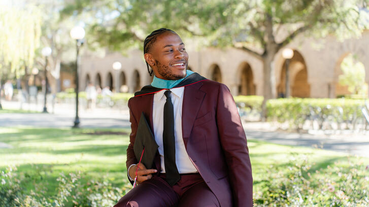 MIP Student Tyler smith posing in a suit and graduation hood in front of a Stanford building recognizable by its arches