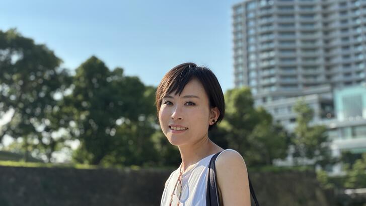 Image of MIP student Yukiko Ueda in a a white tank top with trees and buildings in the background