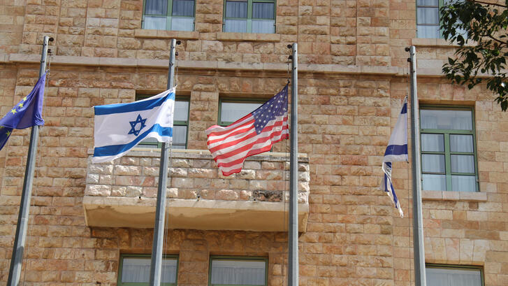 Israeli and American flags flying in front of brick building in Jerusalem.