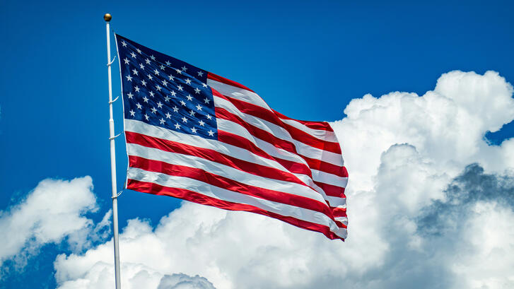 An American flag flying from a white pole against a bright blue sky with large white clouds.