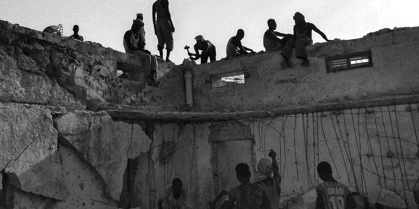 groups of people sitting on and standing near a dilapidated wall