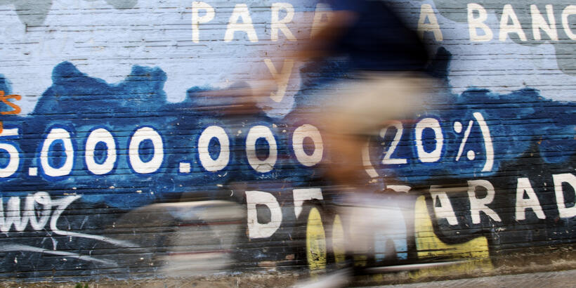 Image of a man riding his bicycle past graffiti about the Spanish bail out and unemployment painted on a wall in Burgos.