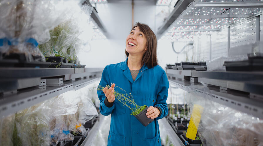 Female researcher holds a plant and looks up optimistically in her lab