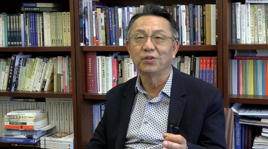 Gi-Wook Shin seated in his office, speaking to the camera during an interview.