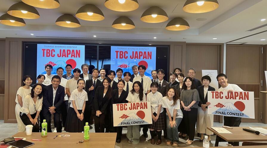 a group of students standing with signs, "TBC Japan"