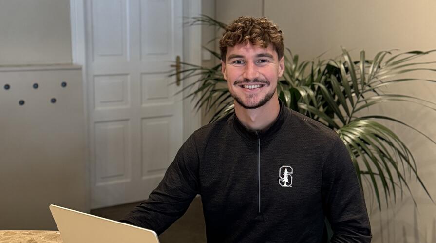 Photo of MIP student Nik White sitting in front of a laptop and smiling