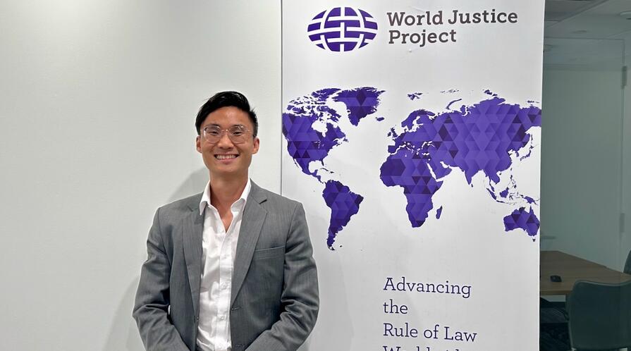MIP student Haolie Jiang posing in front of a World Justice Project banner