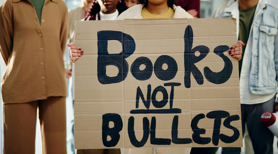 An image of students holding a protest sign that reads "Books not bullets" 