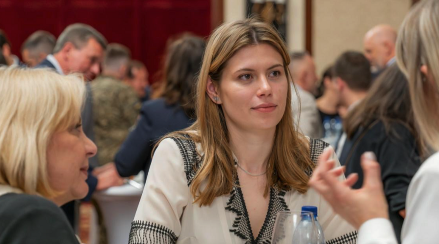Image of MIP Student Sophia Yushchenko sitting at a table in a crowded room, engaged in conversation