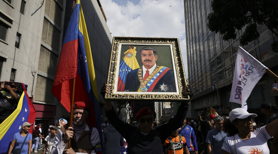 man holds a portrait of nicolas maduro during a march