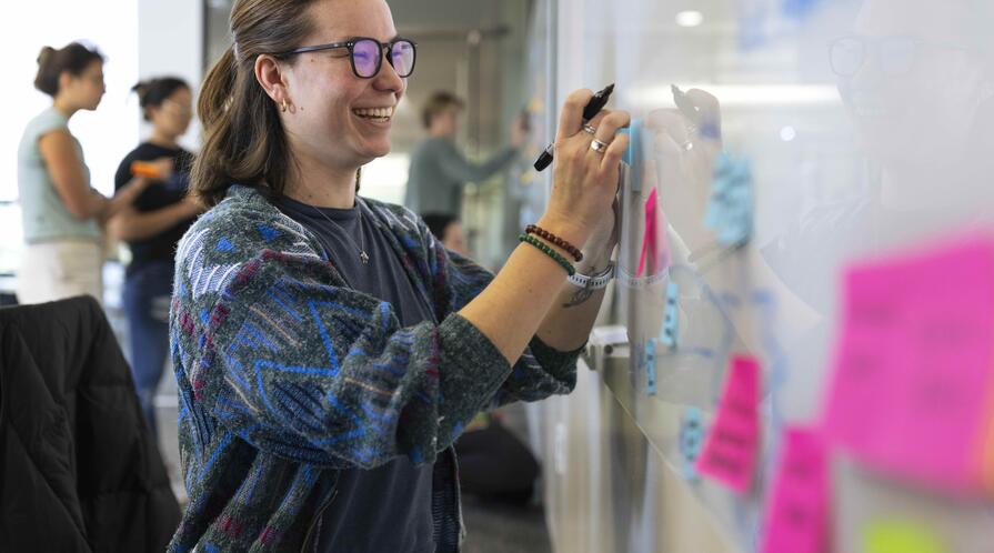 smiling woman standing next to a whiteboard filled with Post-Its