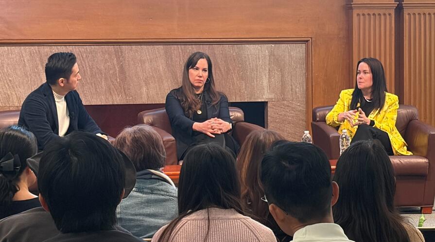 Three speakers during a panel discussion, seated on stage in the Bechtel Conference Center, Stanford University.