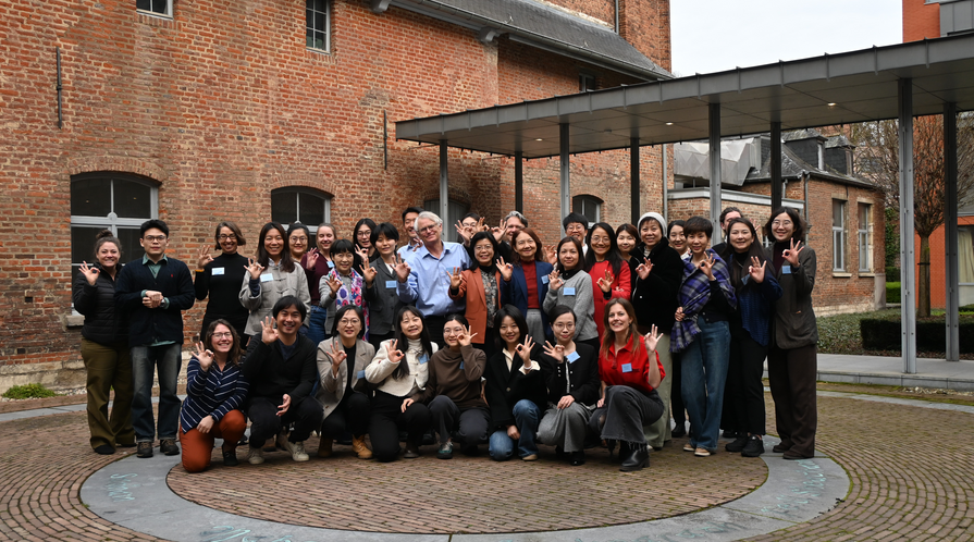A group of conference attendees pose in a courtyard raising hand signs that indication 0 to 3.