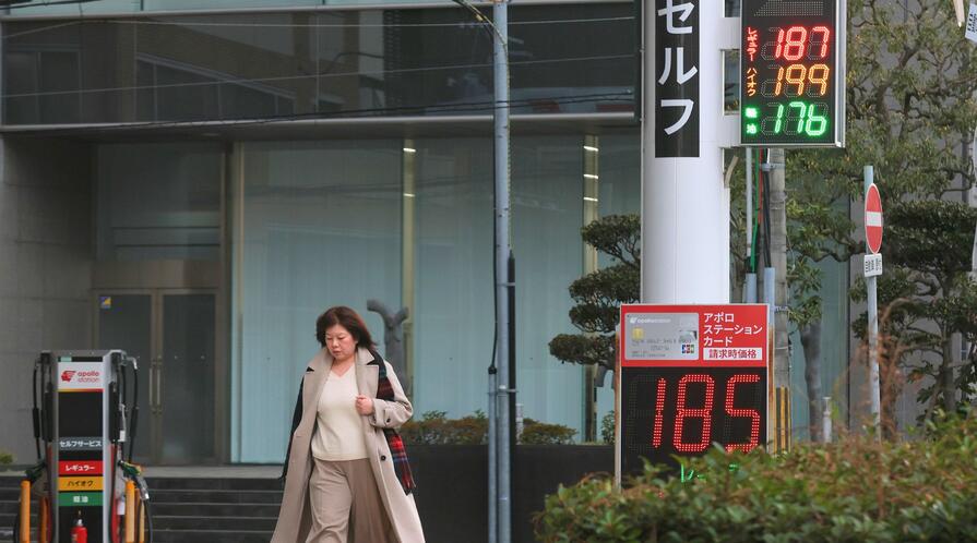 A woman walks past signs displaying gasoline prices outside a gas station on March 13, 2026, in Kobe, Japan. 