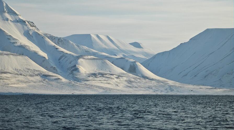 Snow-capped mountains and a seascape on the shore of the Arctic town of Longyearbyen.