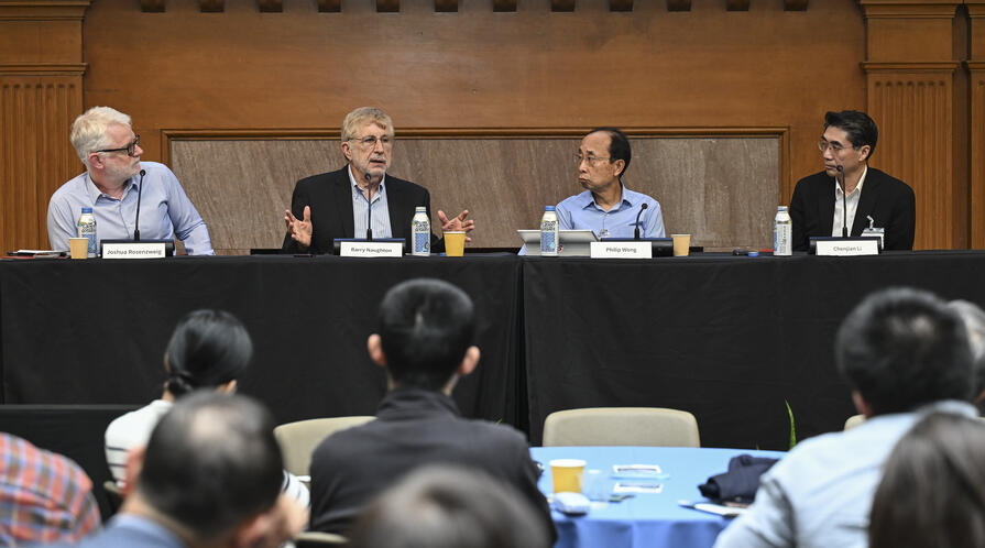 A panel of men sit at a long table on a stage.