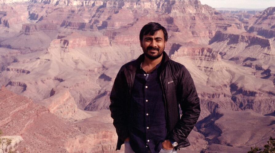 Image of Humzah Khan in a brown jacket, posing in front of the Grand Canyon