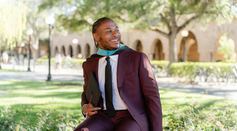 MIP Student Tyler smith posing in a suit and graduation hood in front of a Stanford building recognizable by its arches