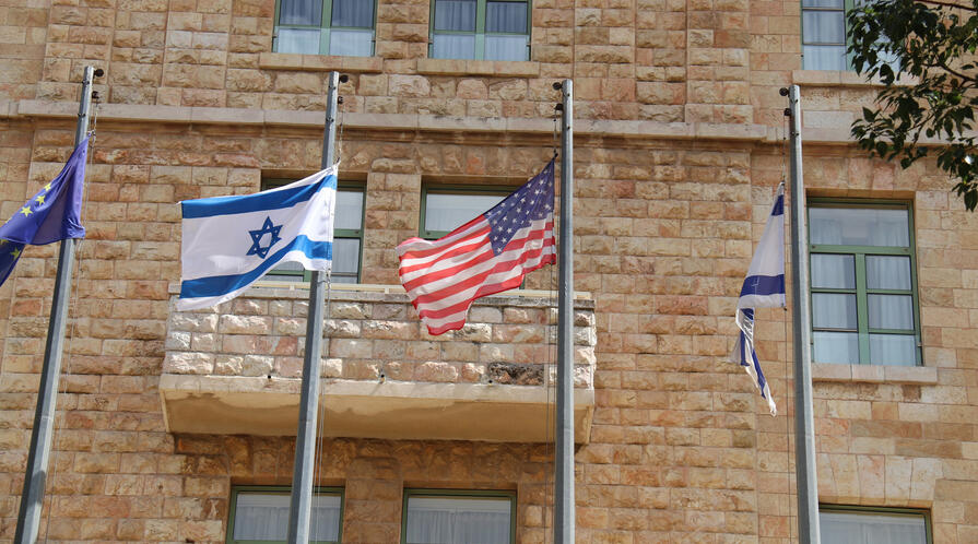 Israeli and American flags flying in front of brick building in Jerusalem.
