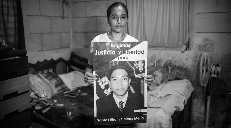 The mother of one of the victims of state terror in El Salvador holding a sign with his photo.