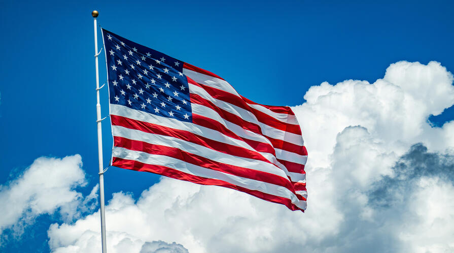 An American flag flying from a white pole against a bright blue sky with large white clouds.