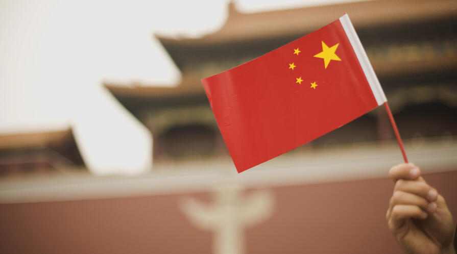 Handheld Chinese flag in front of a government building in Beijing, China.